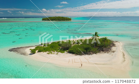 Aerial drone footage of a castaway writing help on the beach of a small desert island with palm trees, surrounded by a turquoise lagoon 117048872