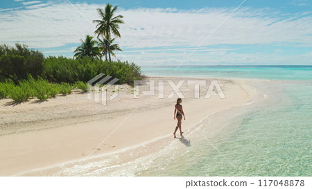 Woman walks on a beautiful maldives beach, enjoying the serene tropical paradise. Palm trees, turquoise waters, and a sunny sky create a peaceful scene Woman walks on a beautiful maldives beach, enjoying the serene tropical paradise. Palm trees, turquoise waters, and a sunny sky create a peaceful scene 117048878