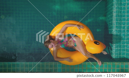 Beautiful woman in bikini relax on bright yellow duck inflatable ring float turquoise swimming pool private villa. Girl relax outdoor lifestyle travel summer holiday vacation. Aerial zoom out Thailand 117048967