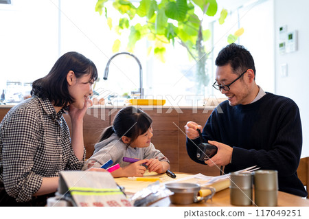 A father teaches his daughter how to use a hand-crank charger for disaster prevention supplies, while a mother watches. 117049251