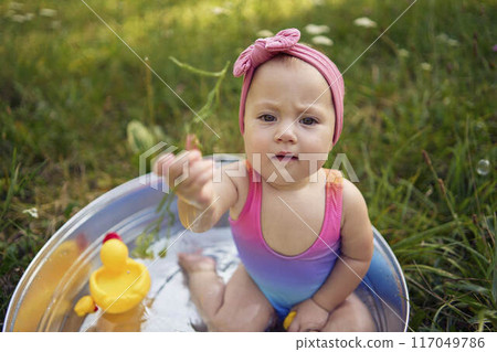 baby in a metal tub plays with rubber ducklings in the summer garden 117049786