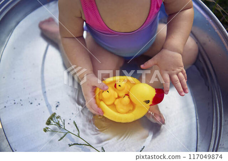baby in a metal tub plays with rubber ducklings in the summer garden baby in a metal tub plays with rubber ducklings in the summer garden 117049874