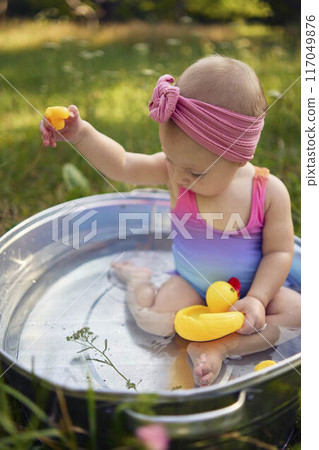 baby in a metal tub plays with rubber ducklings in the summer garden 117049876