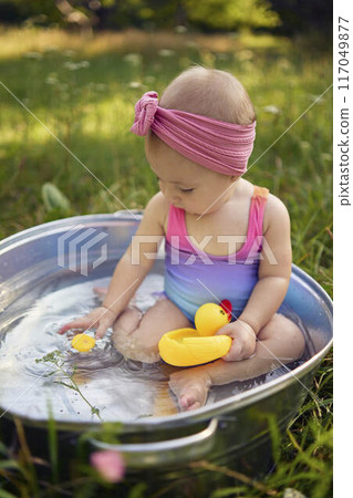 baby in a metal tub plays with rubber ducklings in the summer garden 117049877