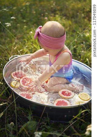 a baby in a metal bath in a summer garden plays with grapefruit and lemon slices a baby in a metal bath in a summer garden plays with grapefruit and lemon slices 117049899