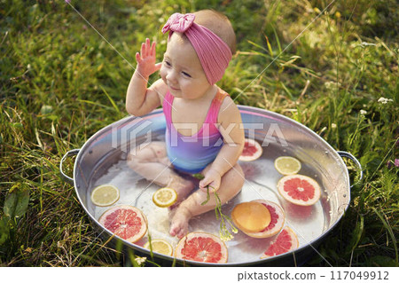 a baby in a metal bath in a summer garden plays with grapefruit and lemon slices 117049912