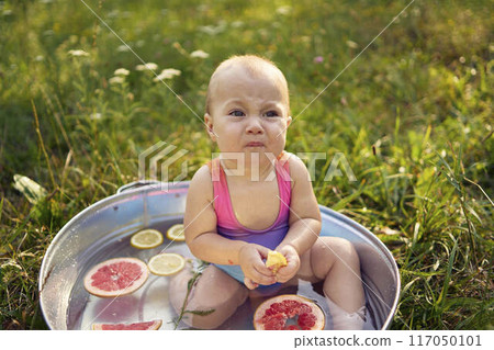 a baby in a metal bath in a summer garden plays with grapefruit and lemon slices a baby in a metal bath in a summer garden plays with grapefruit and lemon slices 117050101