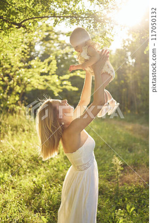 a mother plays with her baby daughter in a sunlit garden 117050132