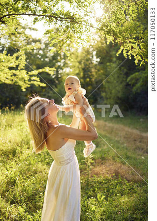 a mother plays with her baby daughter in a sunlit garden a mother plays with her baby daughter in a sunlit garden 117050133