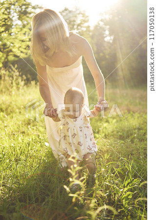 a mother plays with her baby daughter in a sunlit garden a mother plays with her baby daughter in a sunlit garden 117050138