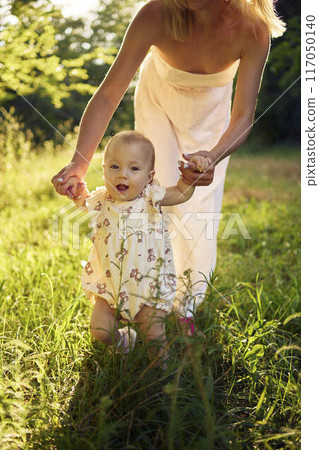 a mother plays with her baby daughter in a sunlit garden a mother plays with her baby daughter in a sunlit garden 117050140