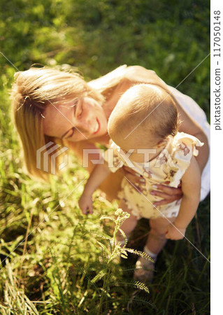 a mother plays with her baby daughter in a sunlit garden a mother plays with her baby daughter in a sunlit garden 117050148