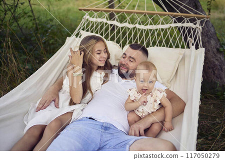 dad playing with his daughters, baby and teenager in a hammock 117050279