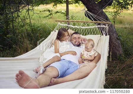 dad playing with his daughters, baby and teenager in a hammock 117050280
