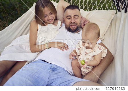 dad playing with his daughters, baby and teenager in a hammock 117050283