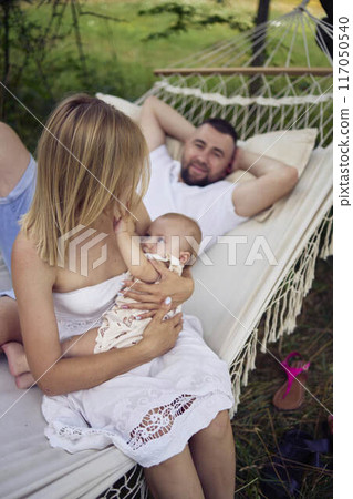 mother is breastfeeding her baby daughter in a hammock, father is lying next to her 117050540