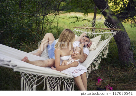 mother is breastfeeding her baby daughter in a hammock, father is lying next to her 117050541