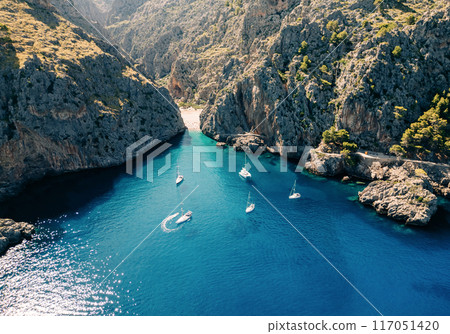 The rocky landscape and the winding road leading to the small, sandy beach nestled between the cliffs 117051420