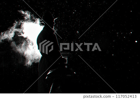 dramatic silhouette of a dangerous man in a hat at night in the rain in the city 117052413
