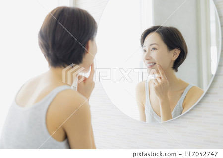 Middle-aged woman looking in the mirror in the bathroom 117052747