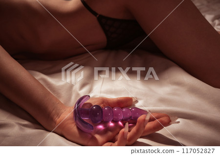 silicone butt anal plug in the female hand of woman girl with a sexy body in panties on bed in bedroom. Female sex toys for anal sex and orgasm silicone butt anal plug in the female hand of woman girl with a sexy body in panties on bed in bedroom. Female sex toys for anal sex and orgasm 117052827