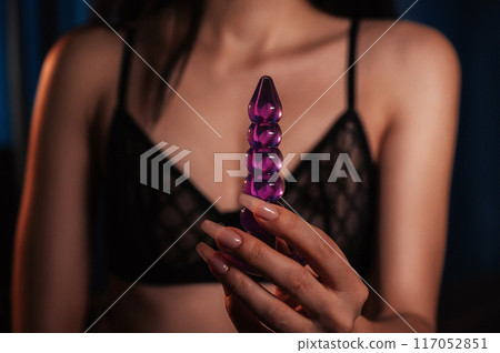 sexy woman holds a silicone anal plug in hands for masturbation and satisfaction. Girl in lingerie with a sex toy for anal orgasm in bedroom close-up 117052851