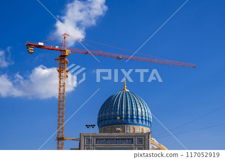 Center of Islamic Civilization in Tashkent, Uzbekistan. Crane on a construction site builds a dome of new large muslim mosque against blue sky background 117052919