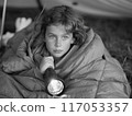 A young girl is lying in a sleeping bag with a flashlight in her hand 117053357