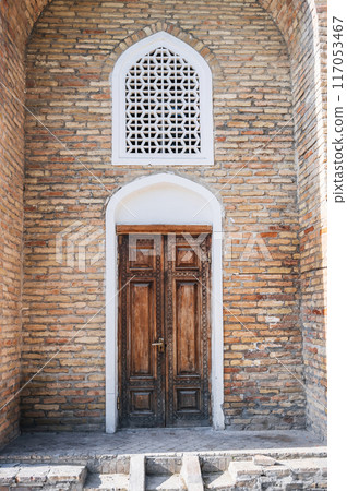 carved wooden door with oriental Uzbek pattern in brick wall in Barak-Khan Madrasah in Tashkent in Uzbekistan 117053467
