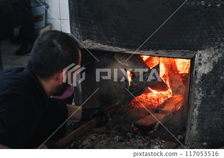 male cook lights a wood-burning stove for large cauldron for cooking Uzbek pilaf in oriental cuisine at Asian restaurant in Uzbekistan male cook lights a wood-burning stove for large cauldron for cooking Uzbek pilaf in oriental cuisine at Asian restaurant in Uzbekistan 117053516