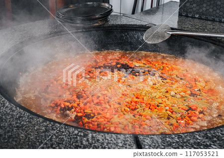 carrots, chickpeas and raisins are boiled in a cauldron to cook traditional oriental Uzbek pilaf in kitchen of a restaurant in Uzbekistan carrots, chickpeas and raisins are boiled in a cauldron to cook traditional oriental Uzbek pilaf in kitchen of a restaurant in Uzbekistan 117053521