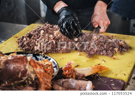 male chef cut boiled lamb meat with a knife to cook asian Uzbek pilaf in restaurant in Central Asian Pilaf Center in Tashkent in Uzbekistan 117053524