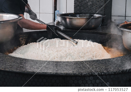 man cook cooking traditional oriental Asian Uzbek rice pilaf in a large cauldron in restaurant in Uzbekistan 117053527