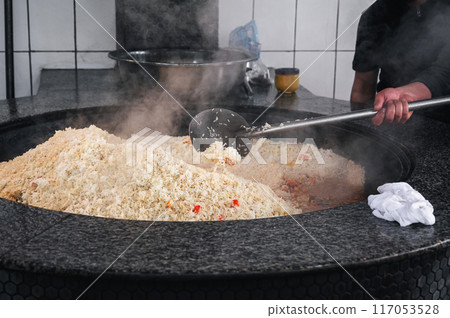male chef prepares traditional Asian Uzbek rice pilaf in large cauldron in kitchen in Uzbekistan 117053528