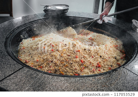 male chef prepares traditional Asian Uzbek rice pilaf in a large cauldron in kitchen of a restaurant in Tashkent in Uzbekistan 117053529