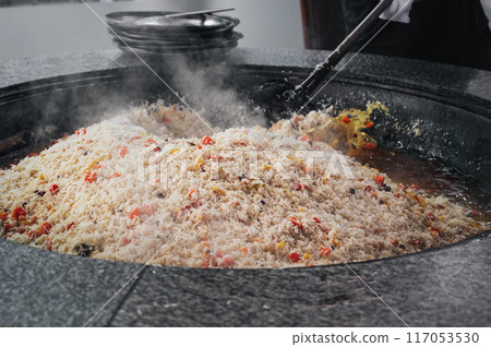 cook cooking traditional oriental Asian Uzbek rice pilaf in large cauldron in kitchen of a restaurant in Tashkent in Uzbekistan 117053530