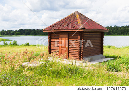 Small wooden hut stands on the lake coast 117053673
