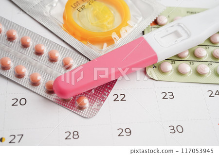 Pregnancy test with birth control pills and condom for female on calendar, ovulation day. Pregnancy test with birth control pills and condom for female on calendar, ovulation day. 117053945