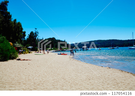 sandy beach on the shore of a blue lake with a pier for boats and yachts 117054116