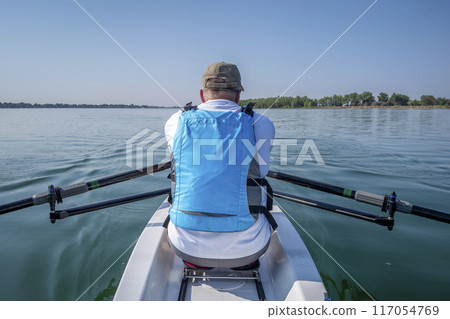 senior male in a rowing shell on calm lake, POV from a boat bow senior male in a rowing shell on calm lake, POV from a boat bow 117054769