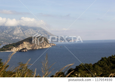 Winter sea colourful landscape with blue water of the Adriatic Sea and the island of St. Nikola near the town of Budva in Montenegro. View from above through the trees. Horizontal Winter sea colourful landscape with blue water of the Adriatic Sea and the island of St. Nikola near the town of Budva in Montenegro. View from above through the trees. Horizontal 117054930