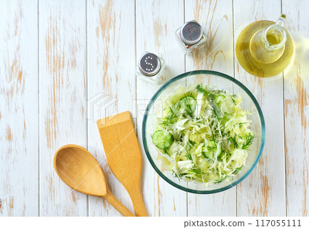 Salad with fresh cabbage and cucumber dill on a white wooden table, top view. 117055111