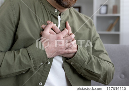 Close-up of man with hands on chest indicating heart pain or heart attack. Concept of health issues, chest pain, and cardiovascular problems. Depicts urgency and medical attention. 117056310