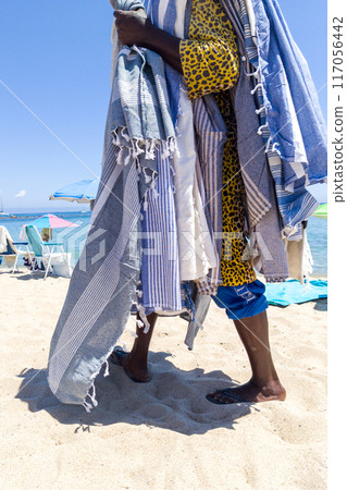 Beach Vendor Draped in Colorful Towels on Sandy Shore Beach Vendor Draped in Colorful Towels on Sandy Shore 117056442