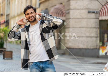 Happy Arabian man taking off wireless headphones and looking at camera smiling in city street 117057740
