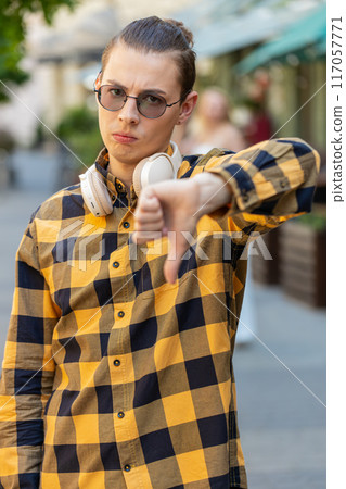 Man tourist showing thumbs down sign gesture, expressing discontent disapproval in urban city street Man tourist showing thumbs down sign gesture, expressing discontent disapproval in urban city street 117057771
