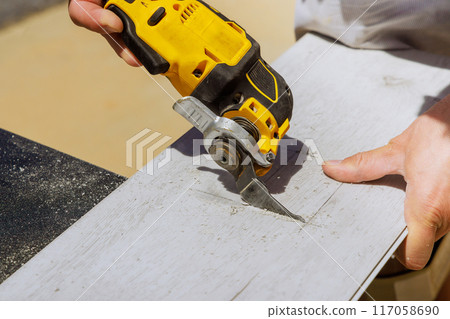 Worker is cutting hole in laminate panel with multitool Worker is cutting hole in laminate panel with multitool 117058690