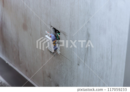 During reconstruction, electrician installs an outlet at wall During reconstruction, electrician installs an outlet at wall 117059233