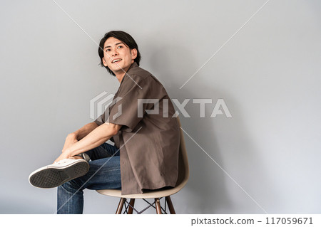 A refreshing man wearing sneakers and jeans sitting on a chair A refreshing man wearing sneakers and jeans sitting on a chair 117059671