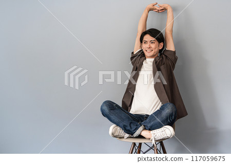 一個穿著運動鞋和牛仔褲的清爽男人坐在椅子上 一個穿著運動鞋和牛仔褲的清爽男人坐在椅子上 117059675